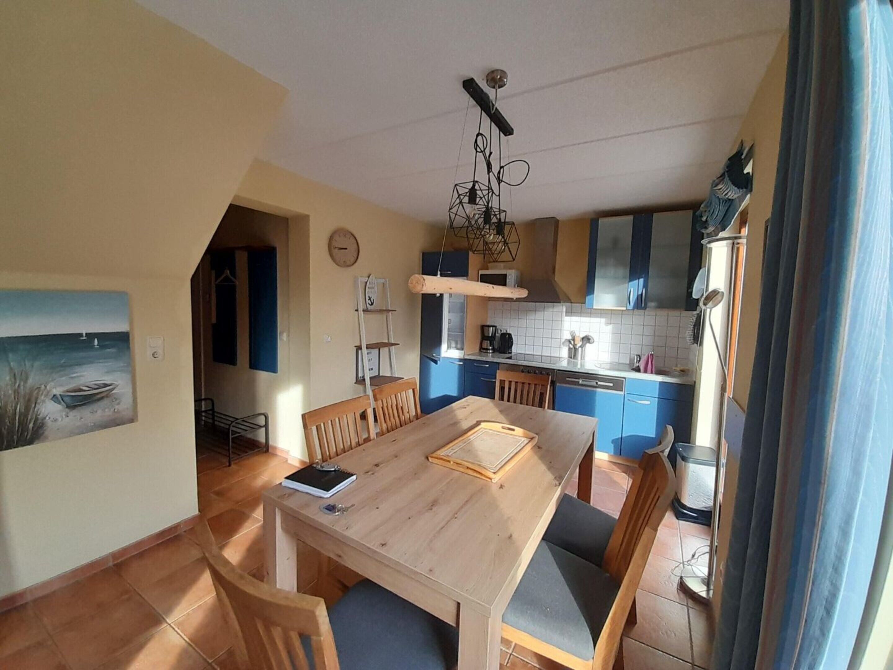 A dining area with a wooden table and chairs, a kitchen with blue cabinets, and a painting on the wall.