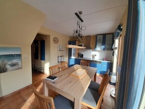 A dining area with a wooden table and chairs, a kitchen with blue cabinets, and a painting on the wall.