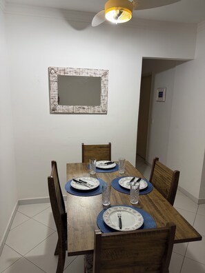 A dining room with a wooden table set for four, equipped with plates, cutlery, and glasses. - Cozy apartment in Guarujá, Enseada beach. (Guarujá)