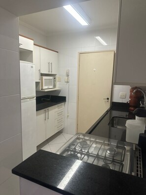 A compact kitchen with white cabinets, a microwave, a gas stove, and a sink. - Cozy apartment in Guarujá, Enseada beach. (Guarujá)