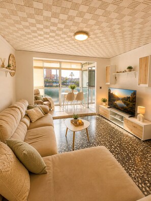 Una sala de estar con sofá, una mesa de centro, televisor y vistas al exterior.