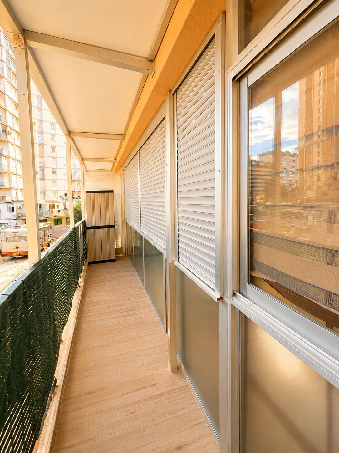 A corridor with a wooden floor, a green safety barrier, and a view of buildings through a window.