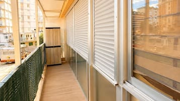 A corridor with a wooden floor, a green safety barrier, and a view of buildings through a window.
