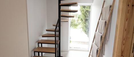 A spiral staircase with wooden steps and black metal railings, leading to a room with a view of greenery outside.