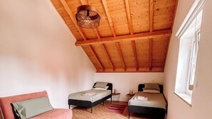 Ett sovrum på entresolplan med ett träpanelat tak, två sängar, en rosa soffa och en vit matta.