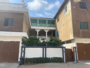A residential building with a balcony, a gated entrance, and a small garden area. - Your cozy home, just a 5-minute walk from the beach (Cotonou)