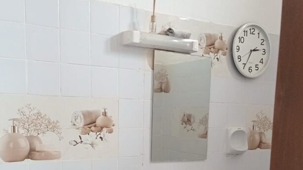 Un baño pequeño con lavadora, un lavamanos, un reloj y azulejos decorativos en la pared.