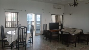 Una sala de estar con televisor, sofá, mesa de comedor, sillas y un balcón.