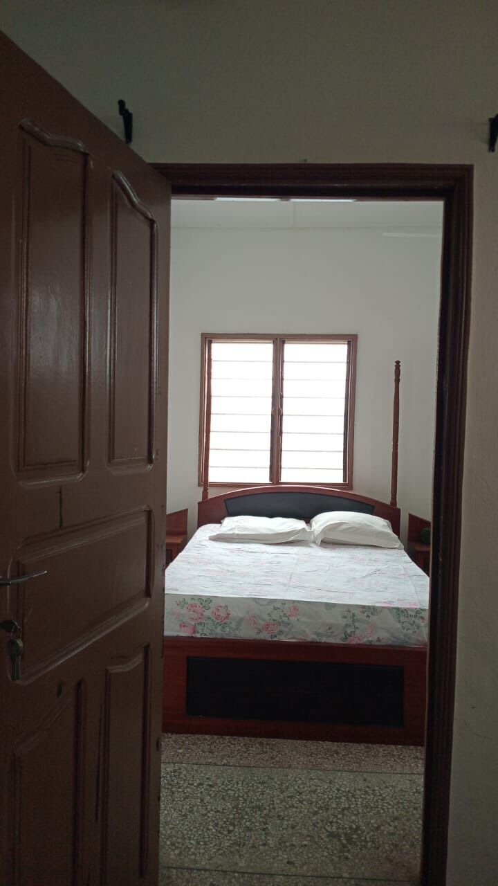 A bedroom with a wooden door, a bed with a floral bedspread, and a window with blinds.