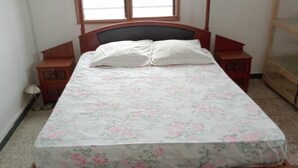 Una cama individual con colcha estampada, una mesita de noche y una ventana con persianas.
