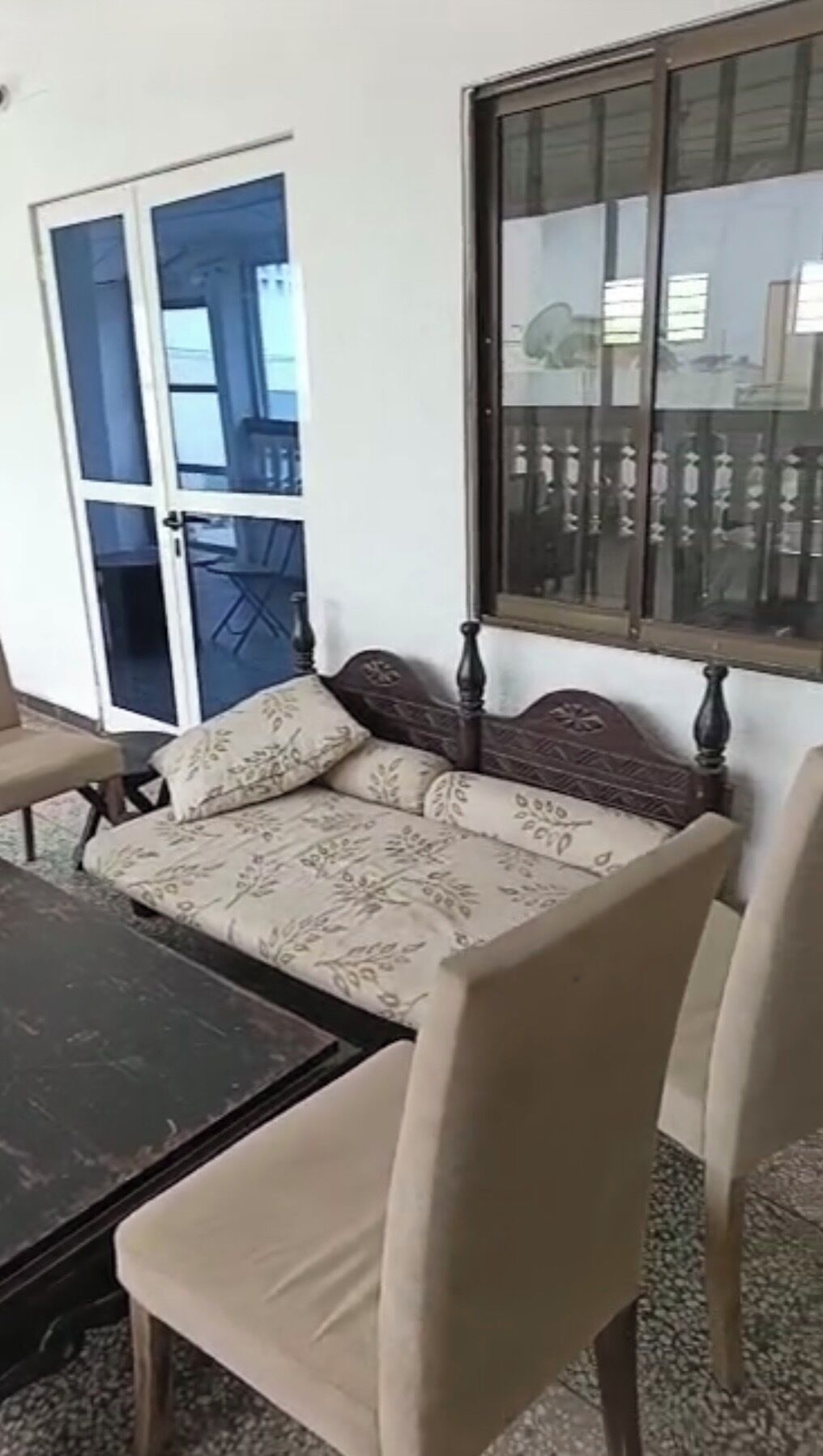 A room with a sofa, two chairs, a table, a window, and a door leading to an outdoor area.