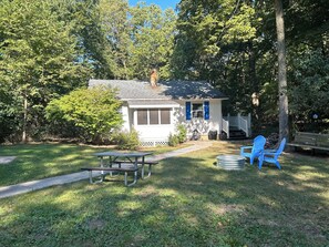 A small house with a porch, a picnic table, and blue chairs in a grassy yard. - Cozy 2-bedroom house in tranquil Put-in-Bay with AC (Put-in-Bay)