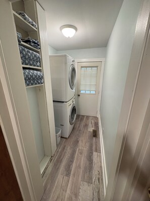 Een wasserette met een wasmachine en droger, een klein raam met luiken, en een houten vloer.