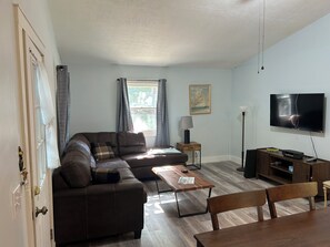 A living room with a sectional sofa, a TV, a lamp, and a dining table.