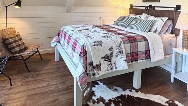 A bedroom with a sloped ceiling, a bed with a plaid blanket, a chair, a lamp, and a cowhide rug.