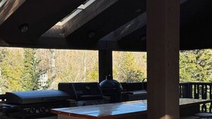 An outdoor kitchen with a grill, bar stools, and a seating area with a wicker chair.