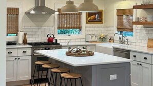 A modern kitchen with a central island, bar stools, pendant lighting, and a stainless steel range hood.