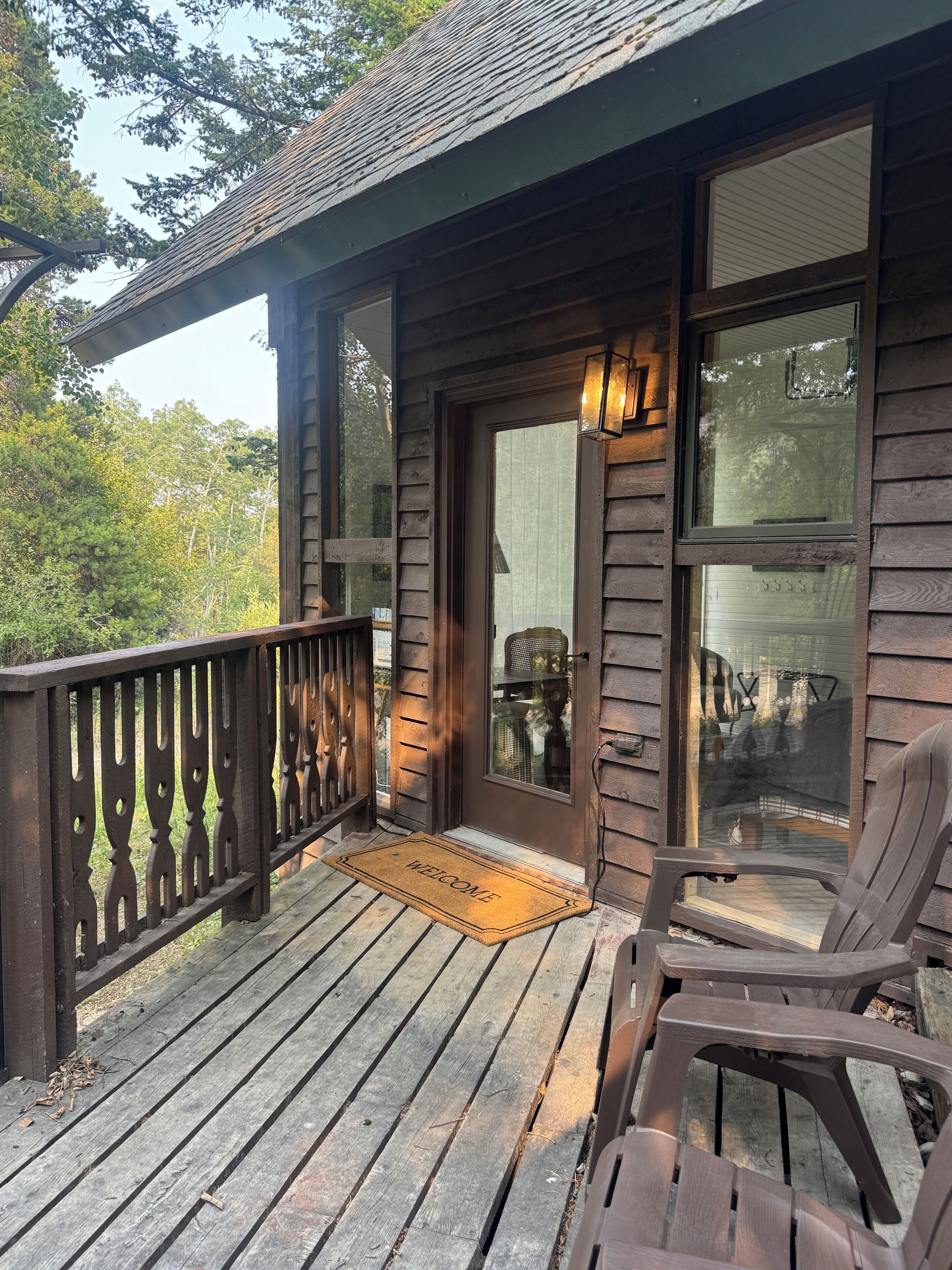 Une véranda en bois avec un paillasson, une chaise et une rambarde.