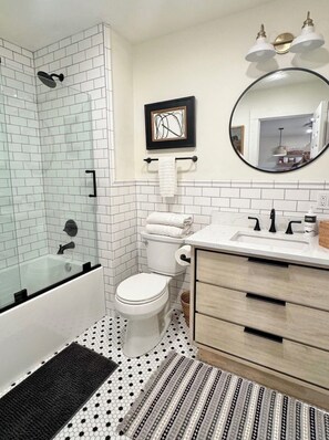 A modern bathroom with a glass-enclosed shower, a toilet, a sink with a mirror, and a patterned rug.