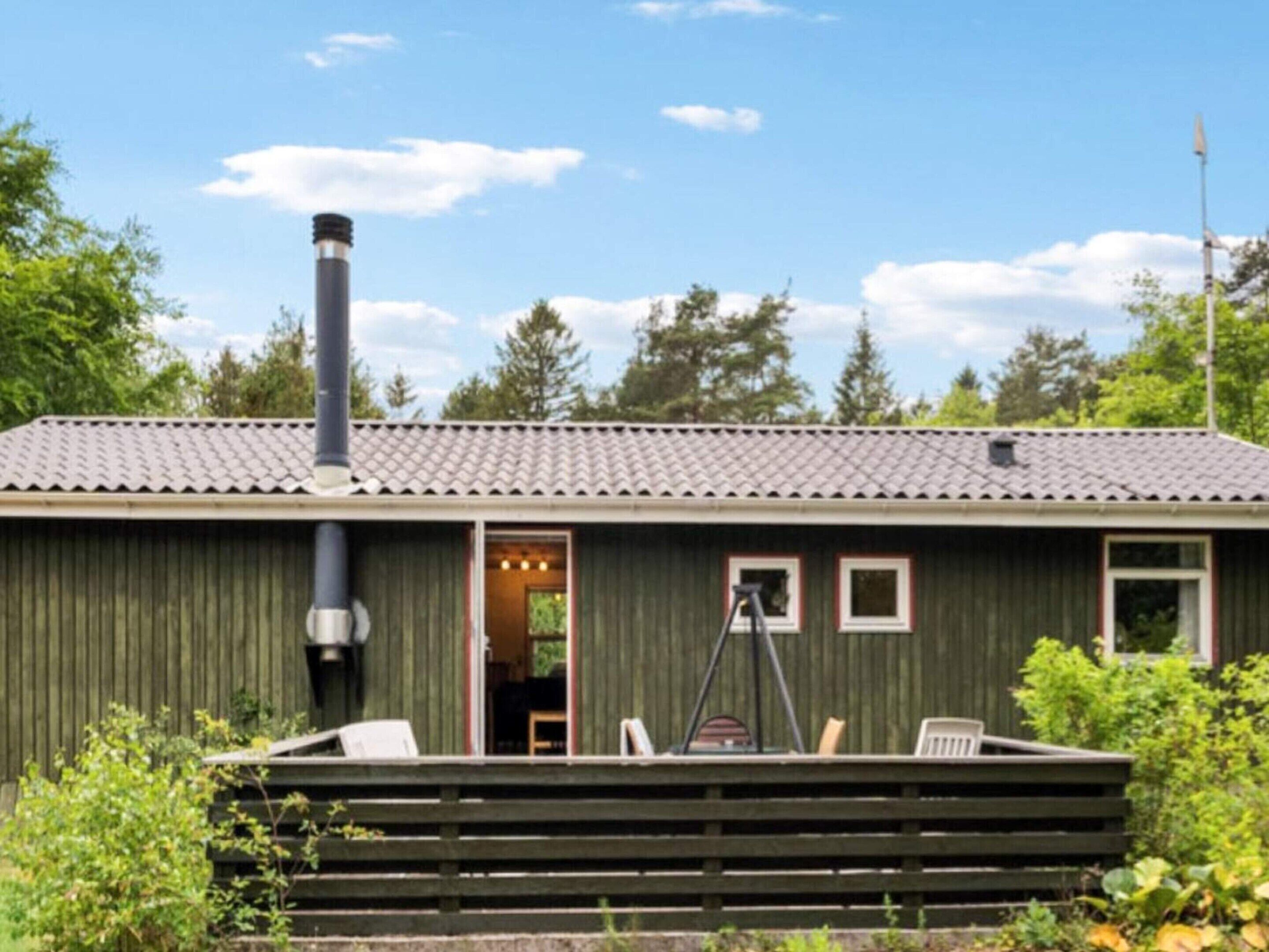 A small building with a chimney, a covered porch with chairs, and a door leading to an interior space.