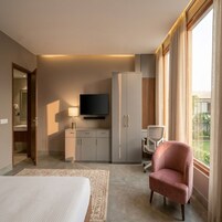 Quarto de hotel com cama, televisão, escrivaninha, cadeira e guarda-roupa.