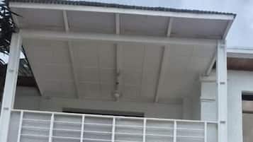 Un edificio de dos plantas con balcón, puertas de cristal grandes y una zona de entrada con tejas.
