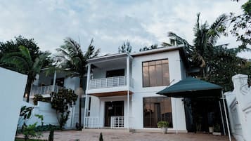 A two-story building with a balcony, a covered entrance, and surrounding greenery.
