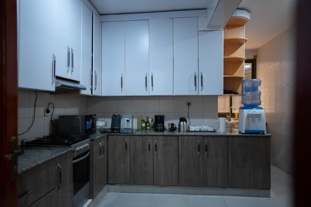 Una cocina con armarios blancos, microondas, cafetera y dispensador de agua.