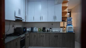 Una cocina con armarios blancos, microondas, cafetera y dispensador de agua.