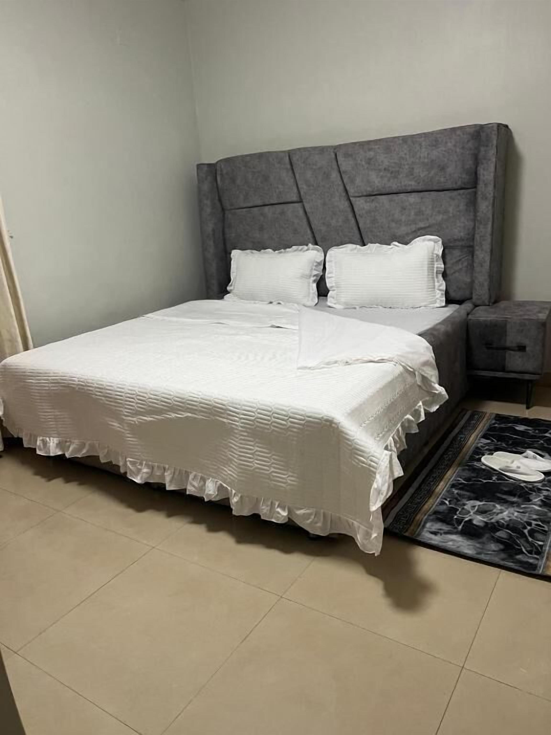 A bed with a grey upholstered headboard, white bedding, and a black and white patterned rug.