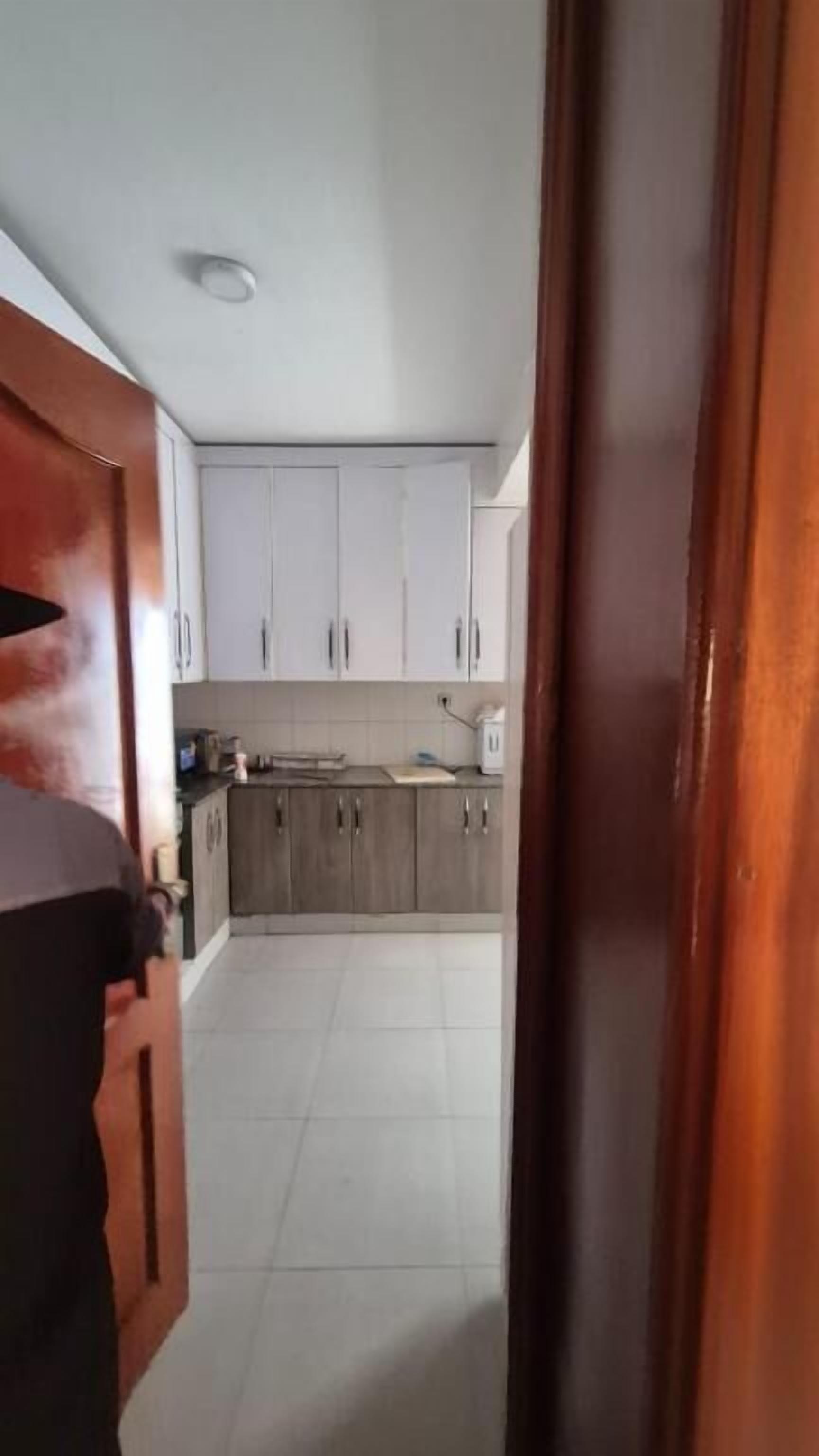 Un pasillo estrecho que conduce a una cocina con armarios blancos y suelo de baldosas.