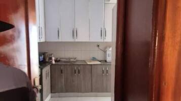 Un pasillo estrecho que conduce a una cocina con armarios blancos y suelo de baldosas.
