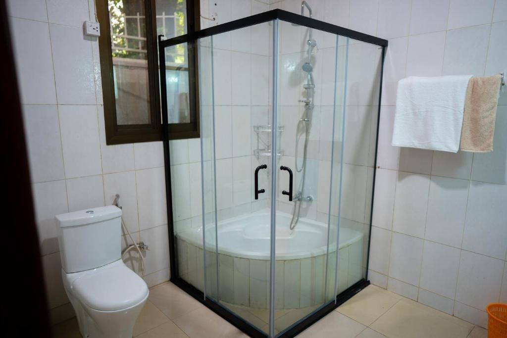 Zona de ducha con paredes de vidrio, un inodoro blanco y un perchero para toallas.