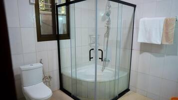 Zona de ducha con paredes de vidrio, un inodoro blanco y un perchero para toallas.