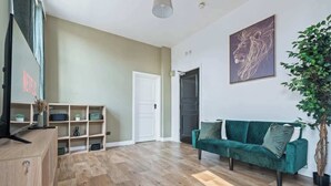 Ein modernes Wohnzimmer mit Holzboden, einem grünen Sofa, einer Pflanze und einer Tür zu einem anderen Raum.