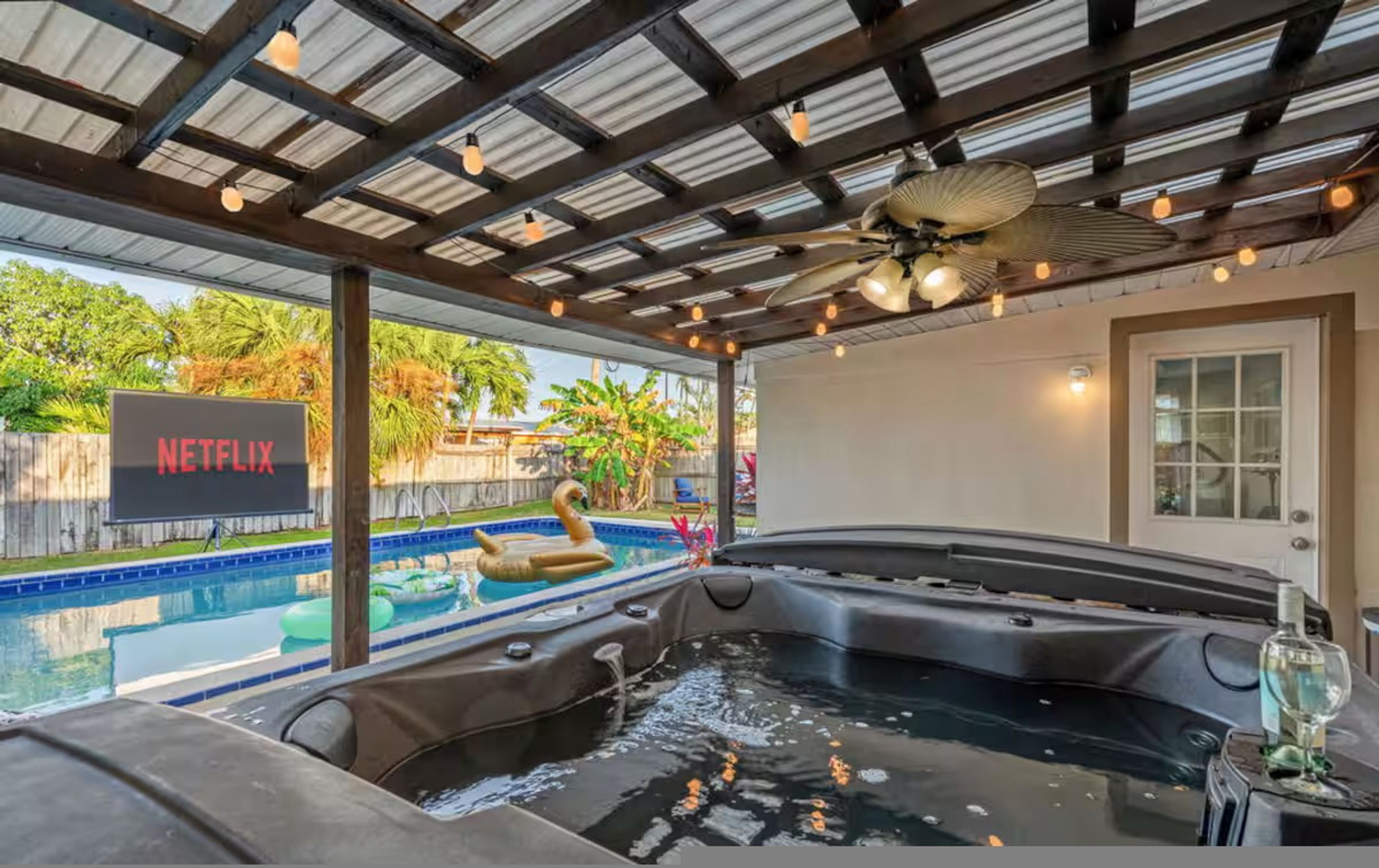 Uma banheira de hidromassagem com vista para a piscina, um ventilador de teto e uma placa indicando Netflix.
