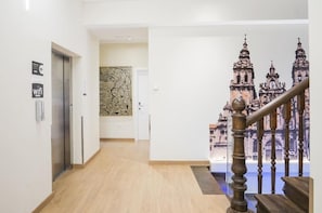 Um corredor com piso de madeira, uma escada com corrimão e uma parede com um grande mural de uma catedral.