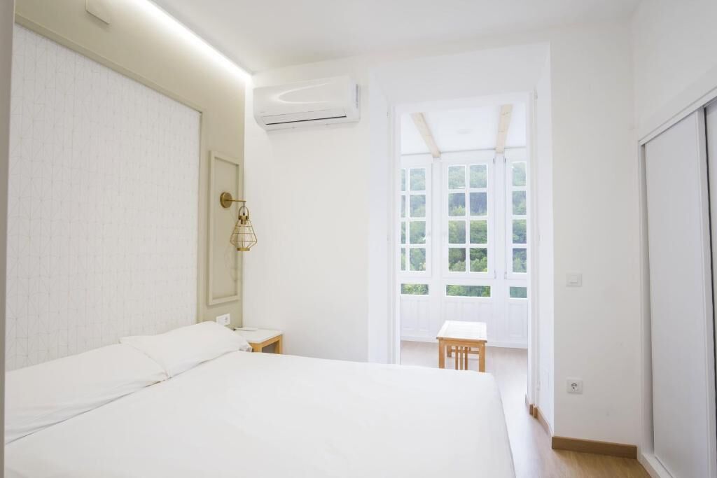 Een slaapkamer met een bed, nachtkastje, airconditioning, raam met uitzicht en een deur.