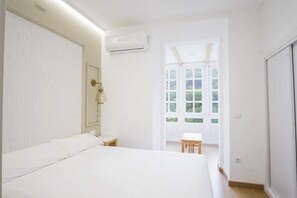 Un dormitorio con cama, mesita de noche, aire acondicionado, ventana con vistas y una puerta.
