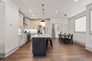 Una cuina moderna amb una illa central, una zona de menjador amb taula i cadires, i una escala que condueix a un altre nivell.
