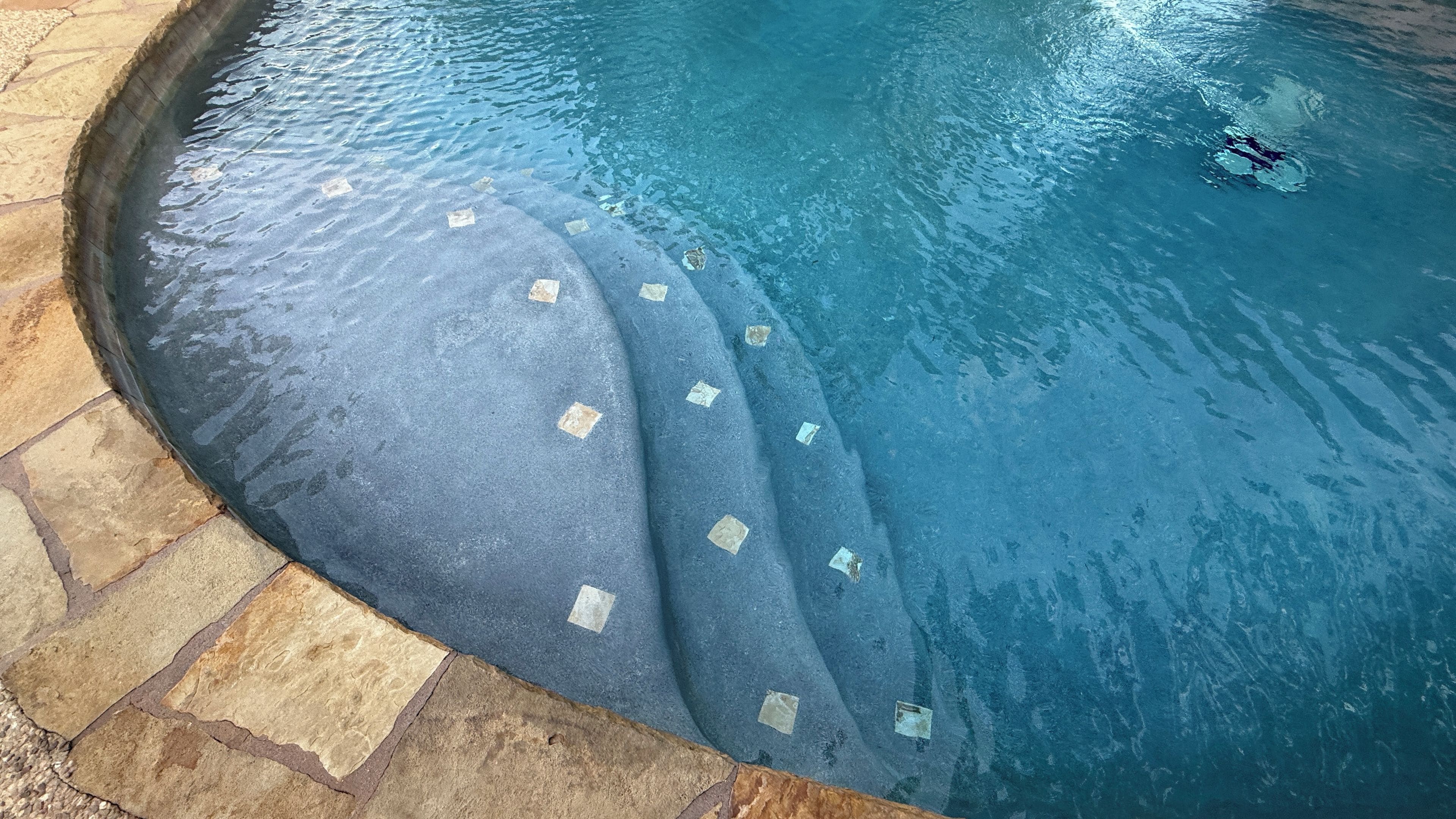 Une piscine bordée de pierres et dotée d’un bord incurvé.