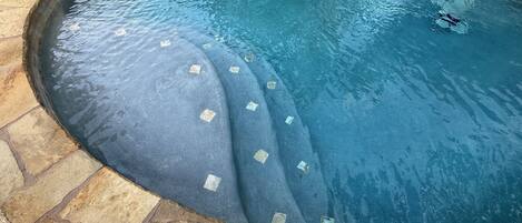 A swimming pool with a stone border and a curved edge.