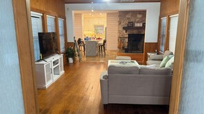 A living room with a grey sofa, wooden flooring, a television, and a kitchen area in the background. - 3-bedroom house in beautiful Spring with amazing Pool (Spring)
