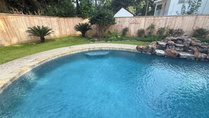 A swimming pool with a curved edge, surrounded by a wooden fence, a grassy area, and a rock feature. - 3-bedroom house in beautiful Spring with amazing Pool (Spring)