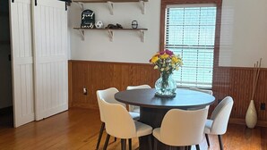 A dining area with a round table, white chairs, a vase with flowers, wooden flooring, a sliding door, and a window with blinds. - 3-bedroom house in beautiful Spring with amazing Pool (Spring)