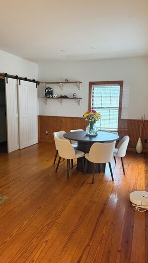 A dining area with a round table, white chairs, a vase with flowers, wooden flooring, a sliding door, and a window with blinds. - 3-bedroom house in beautiful Spring with amazing Pool (Spring)