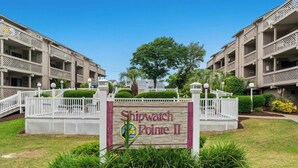 A sign for Shipwatch Pointe II, surrounded by a white fence, with a tree and greenery in the background. - Shipwatch Pointe II Q303 -Indoor Pool -1BR/1BA (Myrtle Beach)