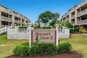 A sign for Shipwatch Pointe II, surrounded by a white fence, with a tree and greenery in the background. - Shipwatch Pointe II Q303 -Indoor Pool -1BR/1BA (Myrtle Beach)