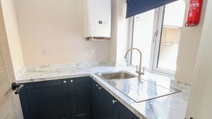 A kitchen with dark cabinets, a marble countertop, a sink, and a window with a view. - The Bungalow (Matlock)