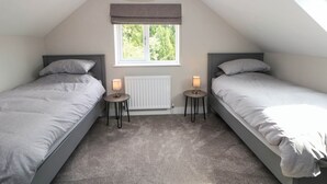 A bedroom with two beds, a window, a radiator, and a ceiling light fixture. - The Bungalow (Matlock)